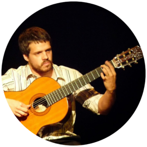 Homem com cabelo e barba castanho-claro, segurando um violão