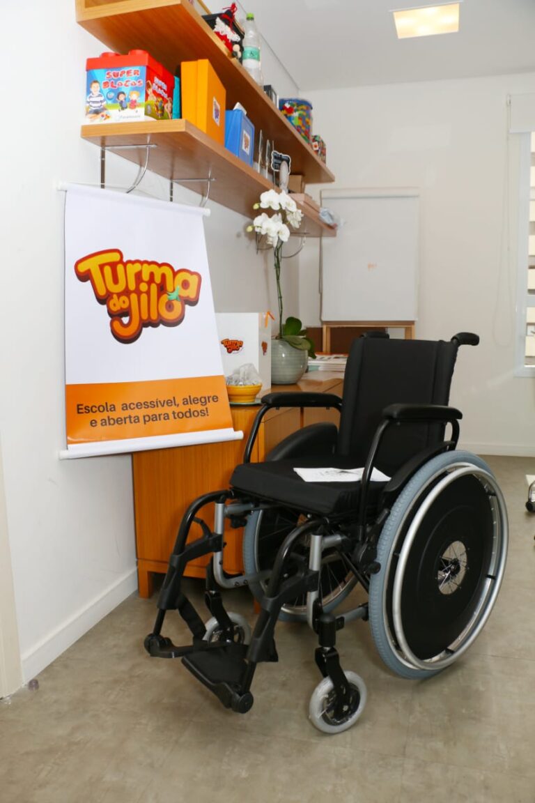 Uma cadeira de rodas ao lado de um cartaz da Turma do Jiló