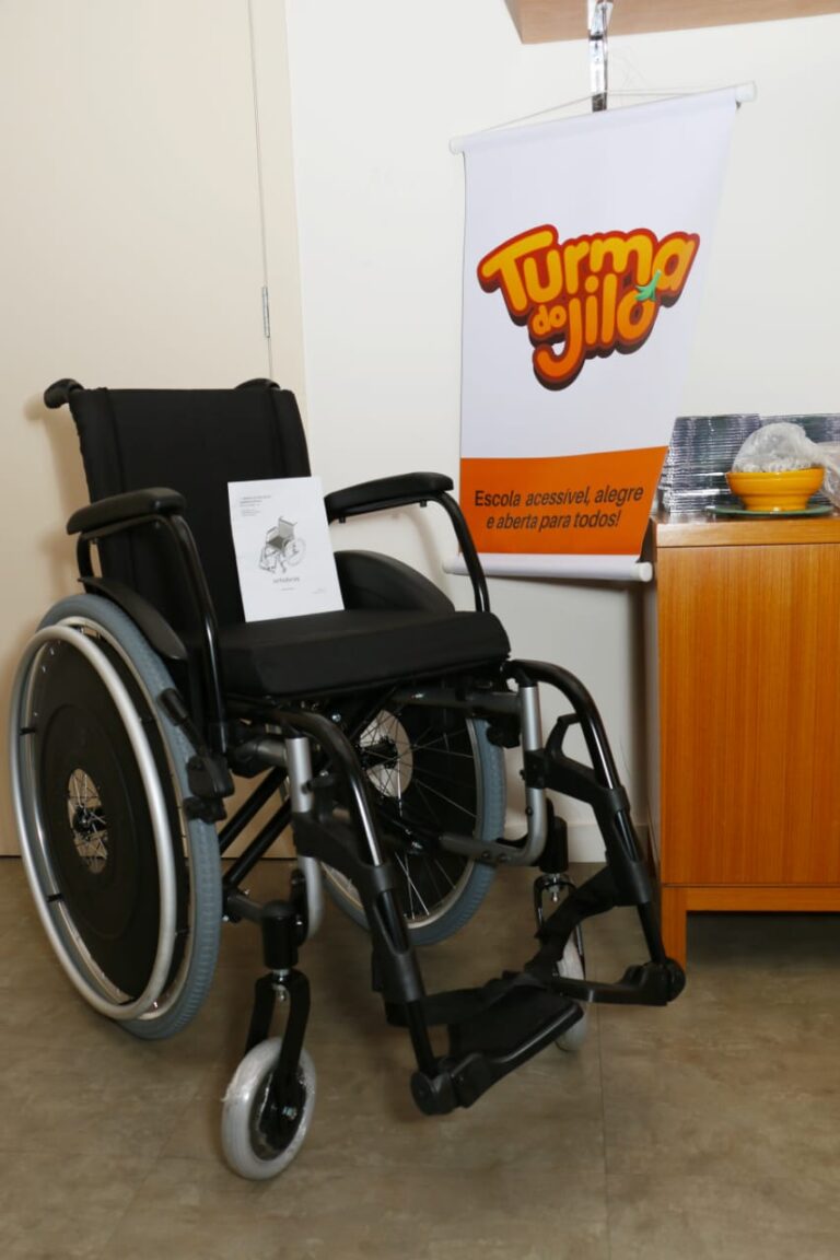 Uma cadeira de rodas ao lado de um cartaz da Turma do Jiló