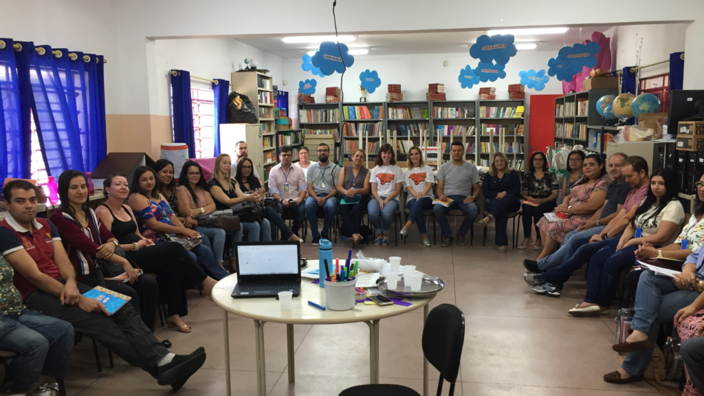 Adultos participantes da Turma do Jiló em círculo em uma biblioteca escolar