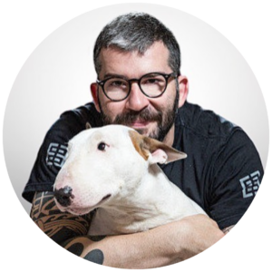 Homem segurando um cachorro branco, com cabelo grisalho e óculos de grau.